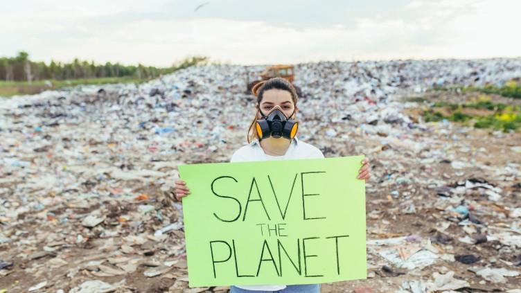Woman in front of a landfill with a sign that says 'Save the Planet'